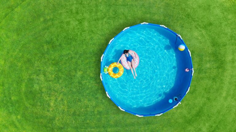 Aerial. Girl swims in a metal frame pool with inflatable toys. Frame pool stand on a green grass law